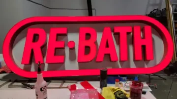 Fabrication of Red Illuminated RE-BATH Channel Letters on Raceway Red illuminated RE-BATH channel letters on a custom oval raceway during final fabrication in the workshop.