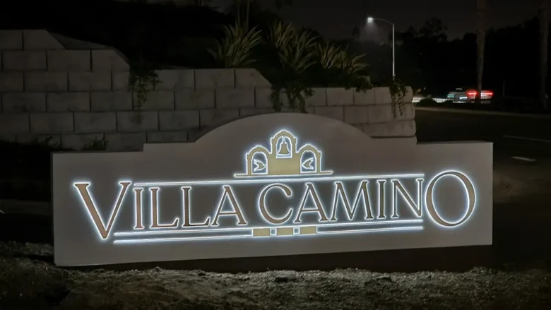 Villa Camino Monument in Oceanside, CA (Solar Powered) Illuminated “Villa Camino” monument sign at night, featuring three decorative arches with bell motifs, set against a landscaped stone wall and street backdrop in Oceanside, California. The sign is solar powered.