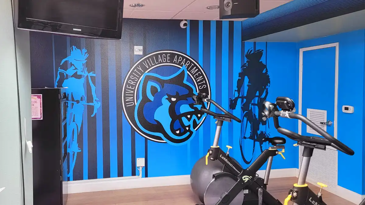 University Village Apartments Cycle Room Wall Graphics CSUSM San Marcos Custom wall graphics installed in the cycle room of University Village Apartments in San Marcos, featuring the blue Cougar mascot logo and silhouettes of cyclists.