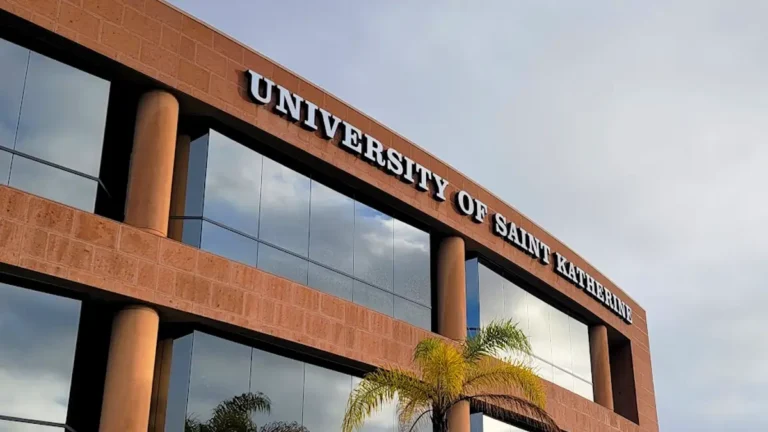 White fabricated channel letters spelling "UNIVERSITY OF SAINT KATHERINE" mounted high on a modern, terracotta-colored office building in San Marcos, CA.